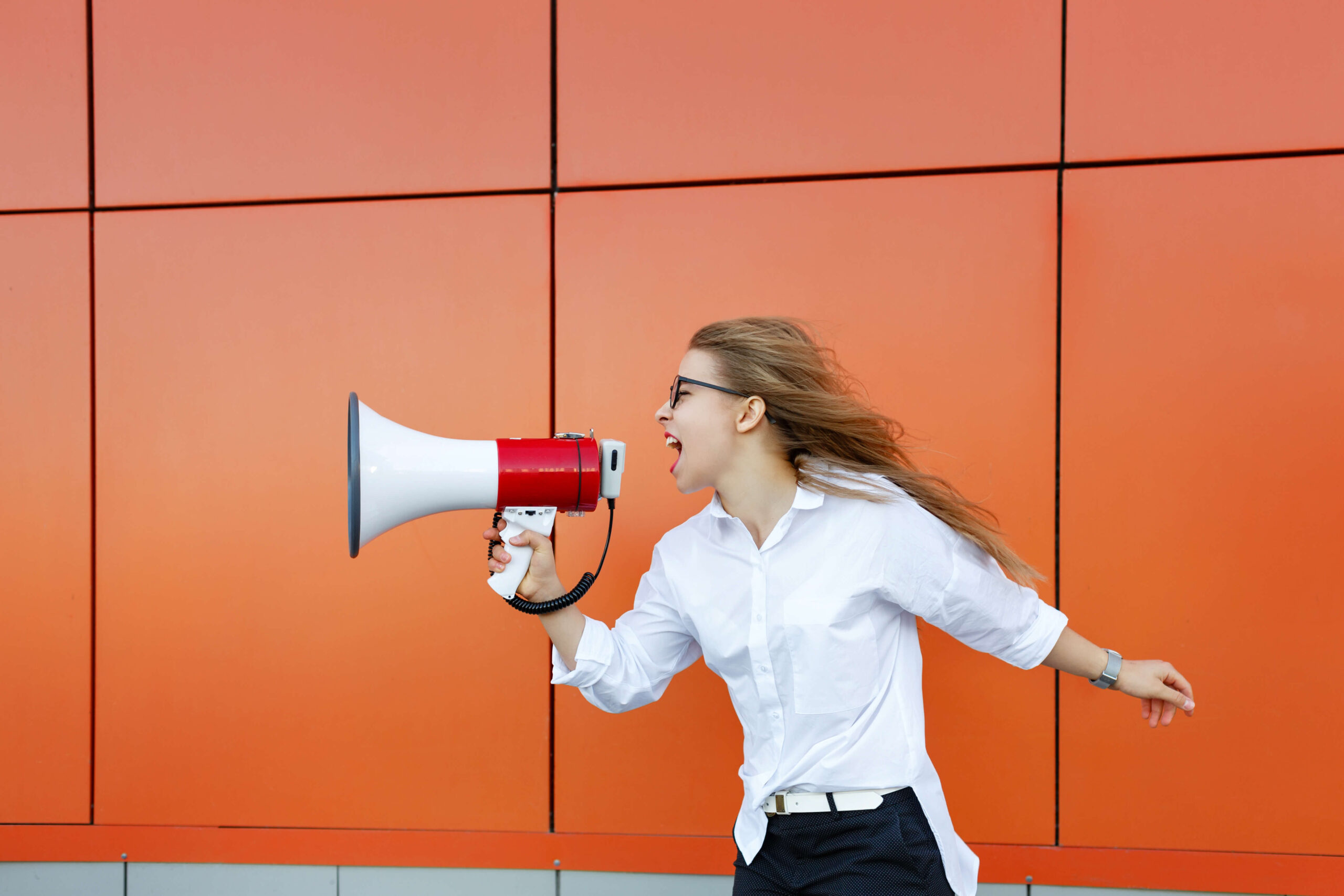 Woman with megaphone against orange wall.